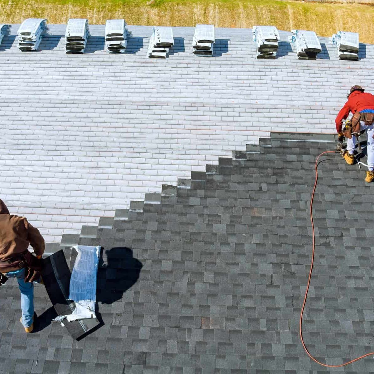 Aerial view in worker hands installing bitumen roof shingles with air hammer and nail